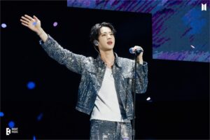 BTS Jin responds to cheers from fans on a stage.