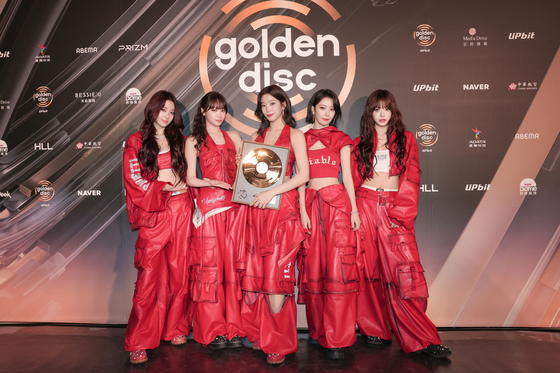 LE SSERAFIM members in red outfits celebrating award win at Golden Disc Awards 2026.