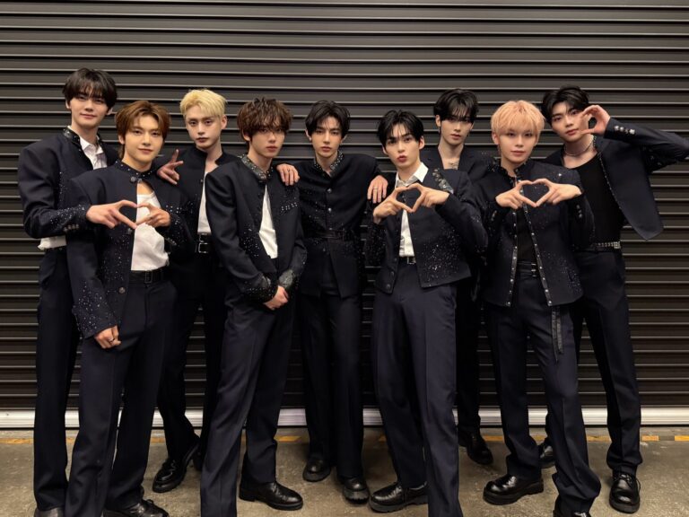ZEROBASEONE full lineup of nine members posing in coordinated black outfits backstage, making heart gestures and showing unity before their encore concert.