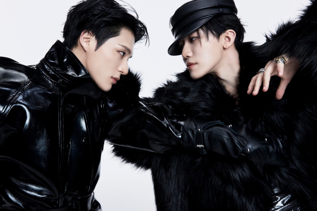 “Black-and-white photo of NCT’s Jeno and Jaemin standing side by side in edgy, futuristic dark outfits against a concrete wall, showcasing confident poses and fashion-forward styling.”