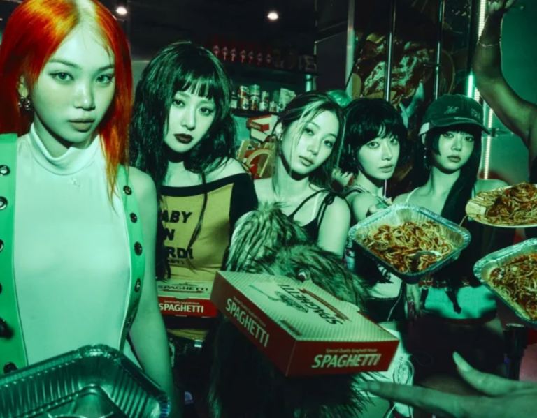 LE SSERAFIM members posing in a stylized restaurant setting, holding spaghetti boxes and trays under dramatic green-tinted lighting, blending fashion with food imagery.