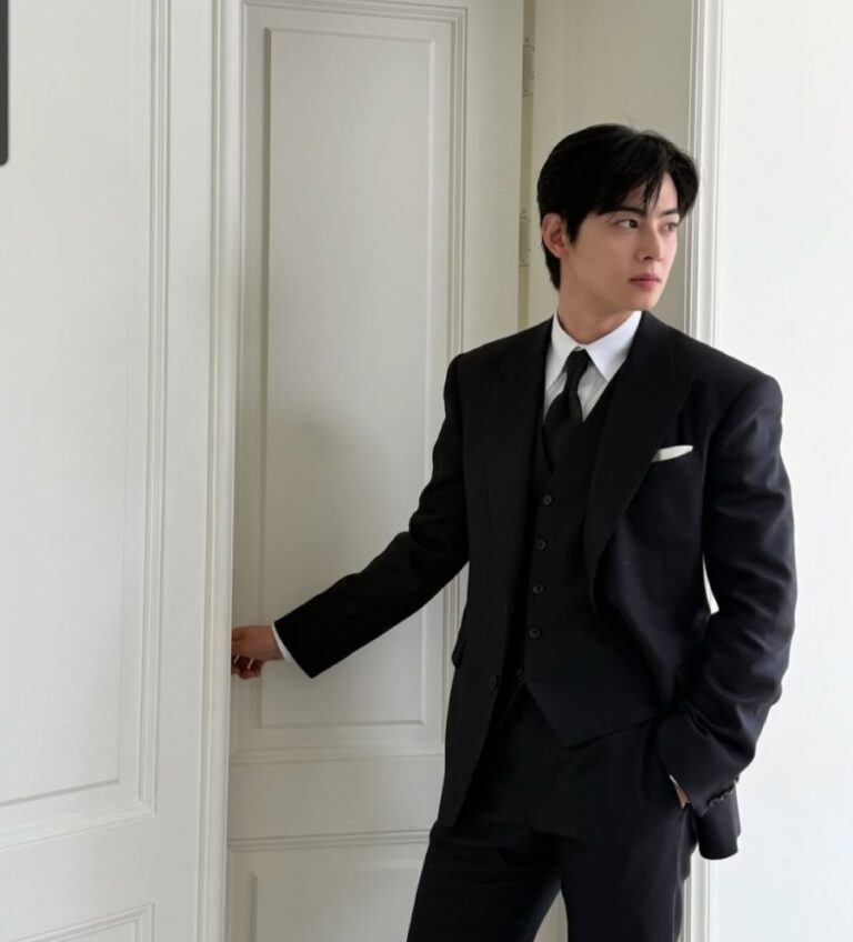 Cha Eun-woo in black three‑piece suit standing by a door.