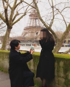 Romantic proposal scene near the Eiffel Tower, with one person kneeling and presenting a ring.