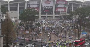 Fans with umbrellas gather outside Goyang Stadium in rainy weather ahead of BTS’s “Arirang” world tour concert.