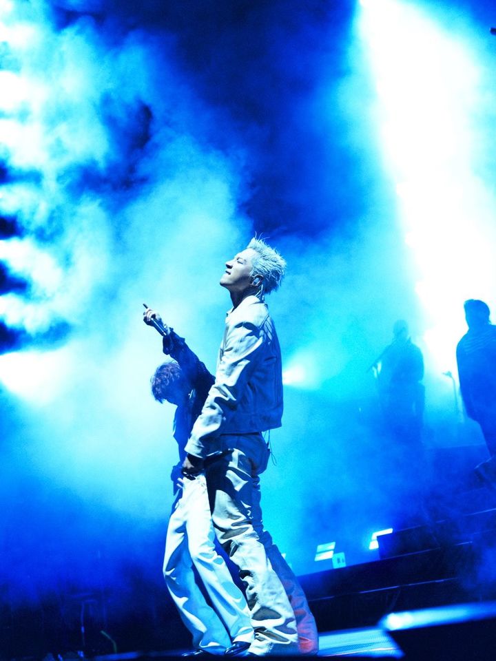 BIGBANG's Taeyang perform on stage under dramatic blue lighting and fog effects.