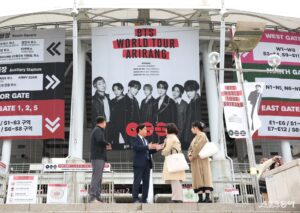 A large BTS “Arirang” world tour poster is displayed at Goyang Stadium entrance as visitors gather and take photos.