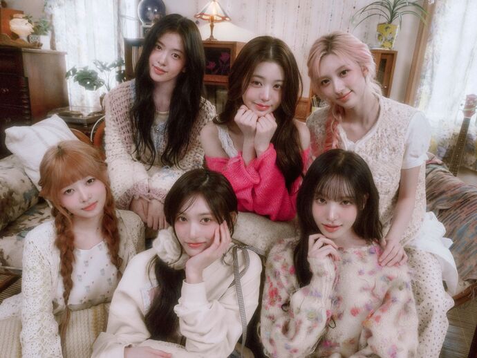 Members of IVE sitting together in a cozy living room, dressed in soft pastel casual outfits.