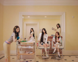 ILLIT members gather in a retro-styled salon room, seated and standing in a coordinated setting.