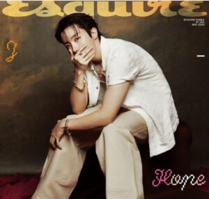 J‑Hope poses on a magazine cover in a white shirt and beige pants, hand partly covering his face.