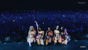 KATSEYE kneels on stage in colorful outfits before a massive Coachella crowd at night.