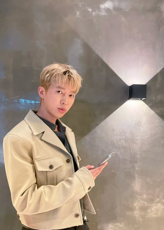 Lim Young‑woong stands with blonde hair and beige jacket under geometric wall lighting.