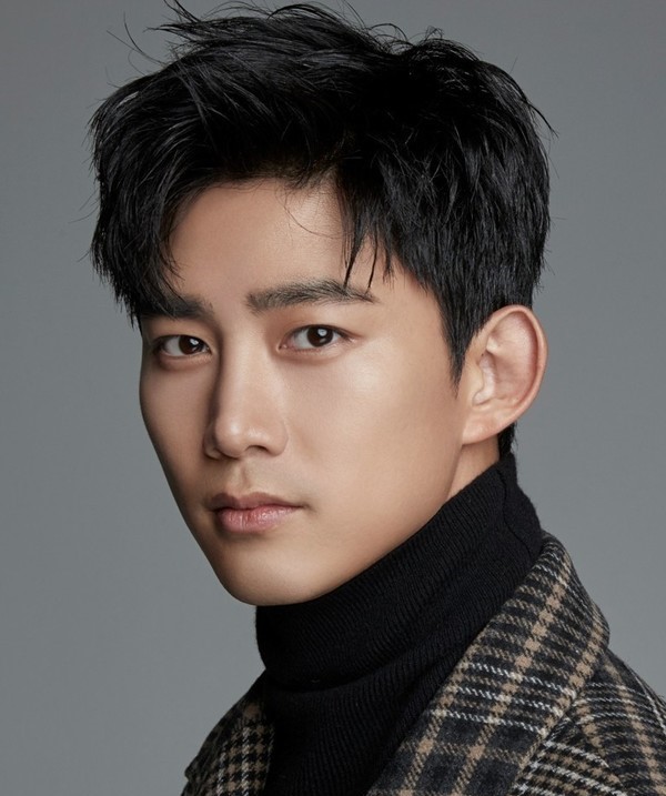 Ok Taecyeon poses in a professional portrait wearing a checkered coat and black turtleneck against a gray background.