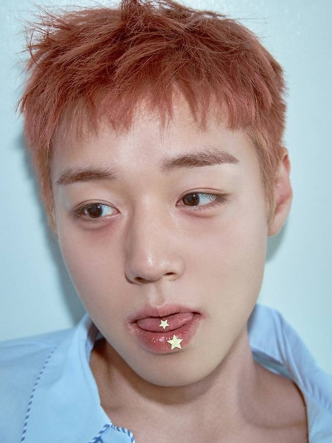 Close-up portrait of Park Ji-hoon with reddish-brown hair and star-shaped decorations on his lips, highlighting his unique artistic style.