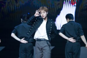 Park Jihoon performs with dancers under colorful stage lights, wearing a black jacket and white shirt.
