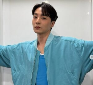 Roy Kim in a bright blue shirt and light blue jacket posing against a plain white background.