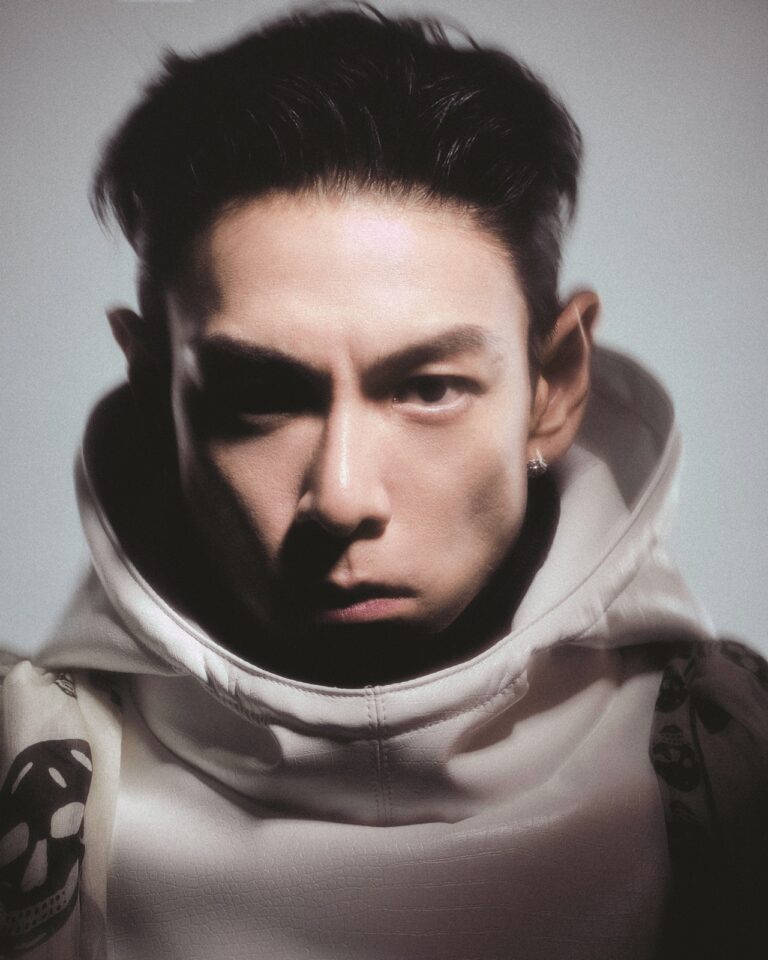 Artistic close-up of T.O.P wearing a hooded garment with skull pattern, lit dramatically