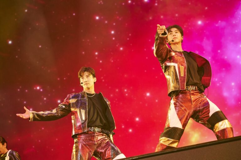 VXQ members perform in metallic outfits under vivid red lighting during their Nissan Stadium show.