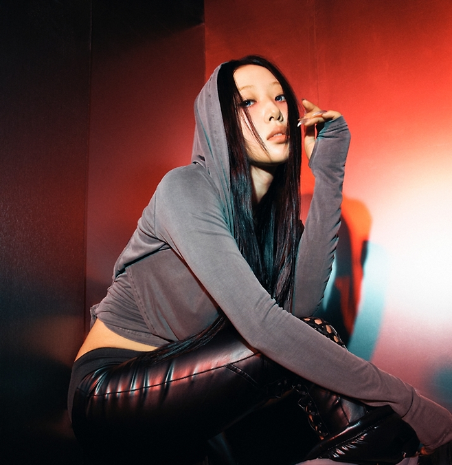 Yves poses in front of a reflective wall with dramatic lighting, wearing a cropped hoodie and leather pants.