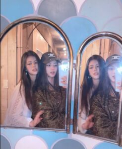 Danielle of NewJeans taking a mirror selfie with her sister, both standing close together in front of arched mirrors.