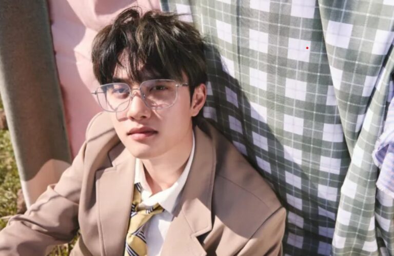 D.O. wears a light brown suit and striped tie outdoors in natural sunlight