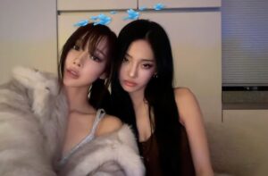 Giselle  and Ningning pose indoors with a fur coat draped over her shoulders, a digital filter adding cartoon birds above her head.