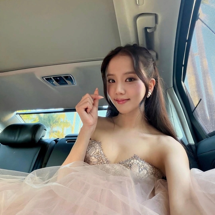 Jisoo sits in a car wearing a strapless lace gown, making a finger‑heart gesture.