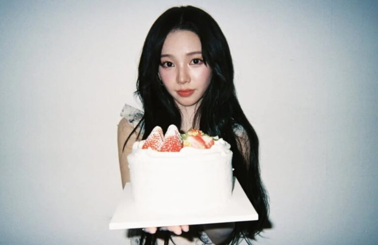 aespa’s Karina holding a strawberry-topped birthday cake, smiling softly against a plain light background.