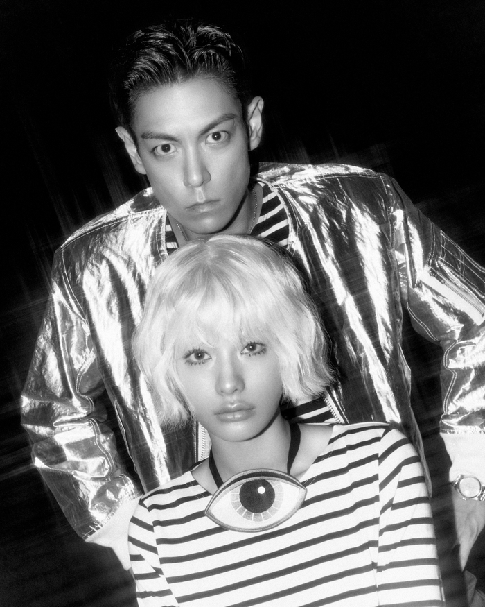 T.O.P and Nana pose together in a black-and-white concept image, with Nana seated in front wearing a striped outfit and T.O.P standing behind in a metallic jacket.