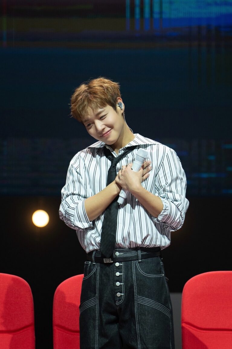 Park Ji-hoon holds a microphone in a striped shirt and tie on stage.