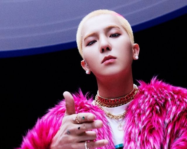 Song Min‑ho poses in a bright pink fur coat with gold necklaces and earrings, hand extended forward.