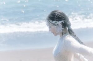 Tiffany Young on the beach with braided hair and floral accessories, dressed in a sheer lace outfit.