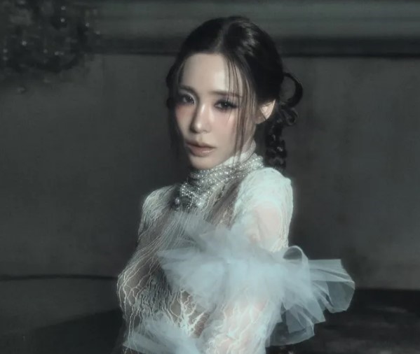 Tiffany Young posing indoors in an elaborate lace and tulle gown with pearl embellishments.