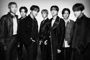 Black-and-white portrait of BTS members standing together in stylish outfits, looking confidently at the camera.