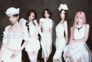 ITZY stands in coordinated white ensembles against a dark backdrop, showcasing unity and bold charisma.