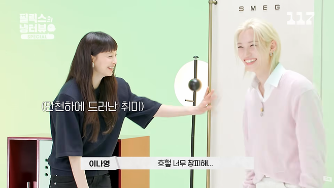 Felix smiles as Lee Na‑young reaches toward him in a mint‑green studio setting.