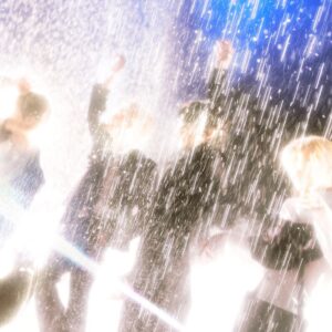 SHINee members stand under heavy rain in bright light, dressed in suits, creating a dramatic and emotional visual.