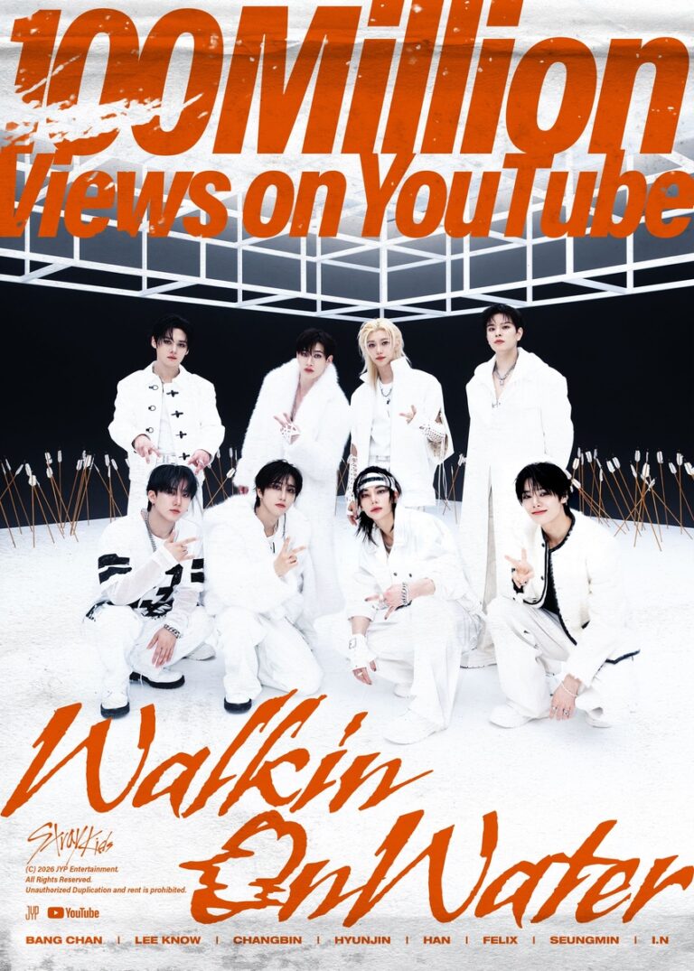 Stray Kids members pose in coordinated white outfits under a geometric frame structure, celebrating 100 million YouTube views for “Walkin On Water.”
