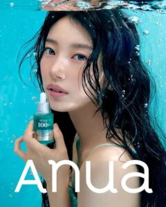 Suzy holds a green Anua 100+ skincare bottle underwater, her hair floating around her face as bubbles rise in the clear blue water.