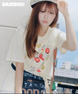 Jeongyeon poses outdoors in Tokyo wearing a printed T-shirt, denim skirt, and light hat, blending casual street style with youthful charm.