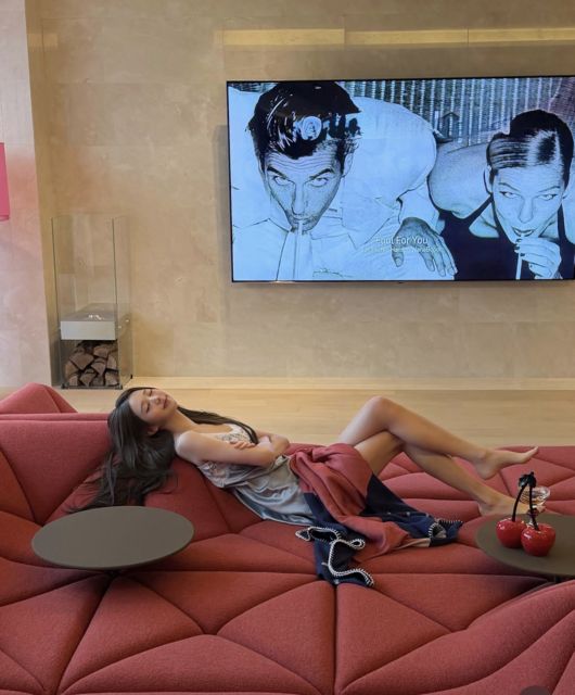 Jang Wonyoung lounging on a red designer sofa in her upscale UN Village home with modern decor and a large wall display.