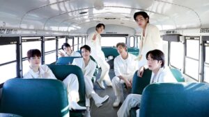 BTS members dressed in coordinated white outfits pose inside a bright bus with teal seats, creating a clean and unified visual composition.