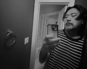 Singer JK Kim Dong‑wook takes a mirror selfie wearing a striped shirt, his expression serious in a dimly lit room.