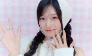 IVE’s Leeseo smiles and waves at the camera while wearing a white knit hat and braided hairstyle.